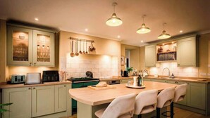 Una cocina moderna con una isla central, taburetes de bar, ollas colgantes y un microondas.