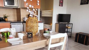 Et moderne køkken med orange skabe, en mikrobølgeovn, et spisebord med stole og et fjernsyn i baggrunden.