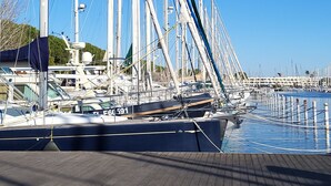 Ein Yachthafen mit mehreren Segelbooten, ein klarer, blauer Himmel und ein gepflasterter Weg im Vordergrund.