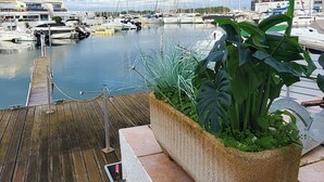 Ein Yachthafen mit vertäuten Booten, ein Holzdeck und ein Pflanzgefäß mit Grünpflanzen.