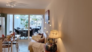 Ein Wohnzimmer mit einer Couch, einem Couchtisch und einer Lampe. Es gibt einen Essbereich mit Stühlen und einem Tisch. Das Zimmer bietet einen Ausblick nach draußen.