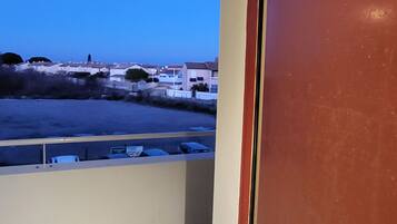 Vista de um quarto com uma porta identificada como “C-19”, em direção a uma área de estacionamento e edifícios ao longe.