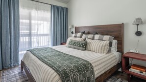 Una camera da letto con un letto, tende, un comodino, una lampada e vista sull'esterno.