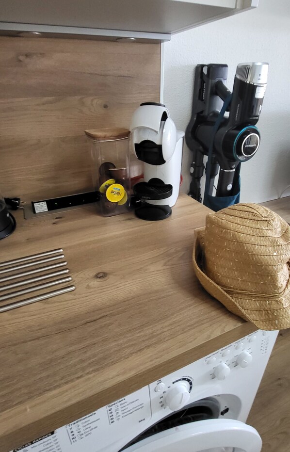 Eine Küchenzeile mit Kaffeemaschine, Staubsauger, Strohhut und Herd.