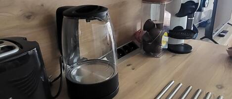 Un comptoir de cuisine avec une machine à café, un récipient en verre doté d’un couvercle et plusieurs tiges métalliques.