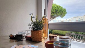 Ein Tisch mit einem Kartenspiel, einem Glas Wasser, einer Flasche und einem Blumentopf auf einem Balkon mit Blick auf Gebäude und Bäume.
