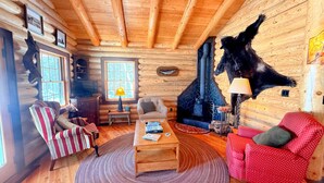 Ein Blockhaus-Interieur mit Kamin, Sesseln mit Streifenmuster und einem roten Musterstuhl sowie einem Fernseher.