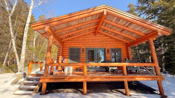 A log cabin with a covered porch, a dining area, and a fireplace.