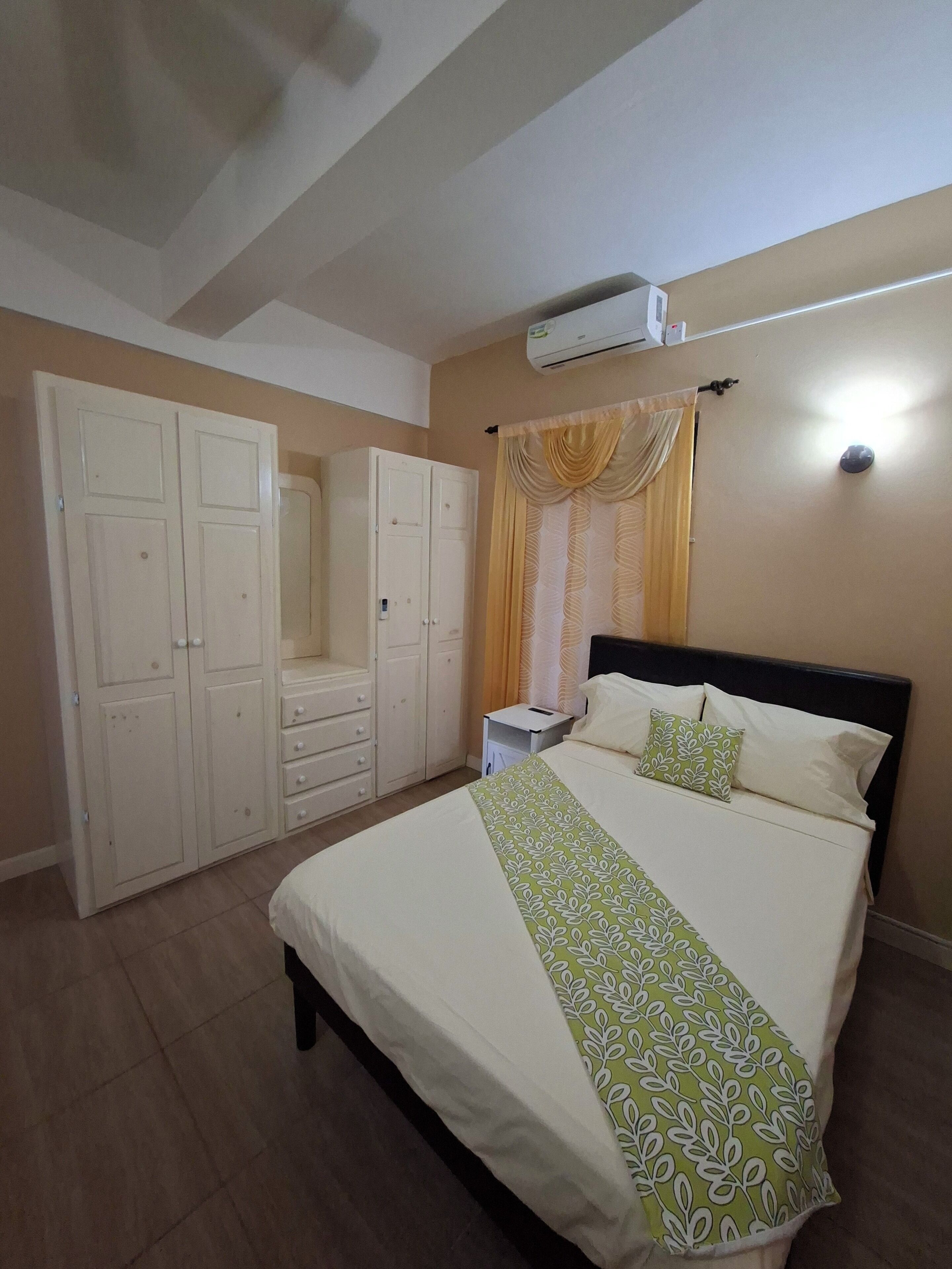 Un dormitorio con cama, armario, mesita de noche y unidad de aire acondicionado.