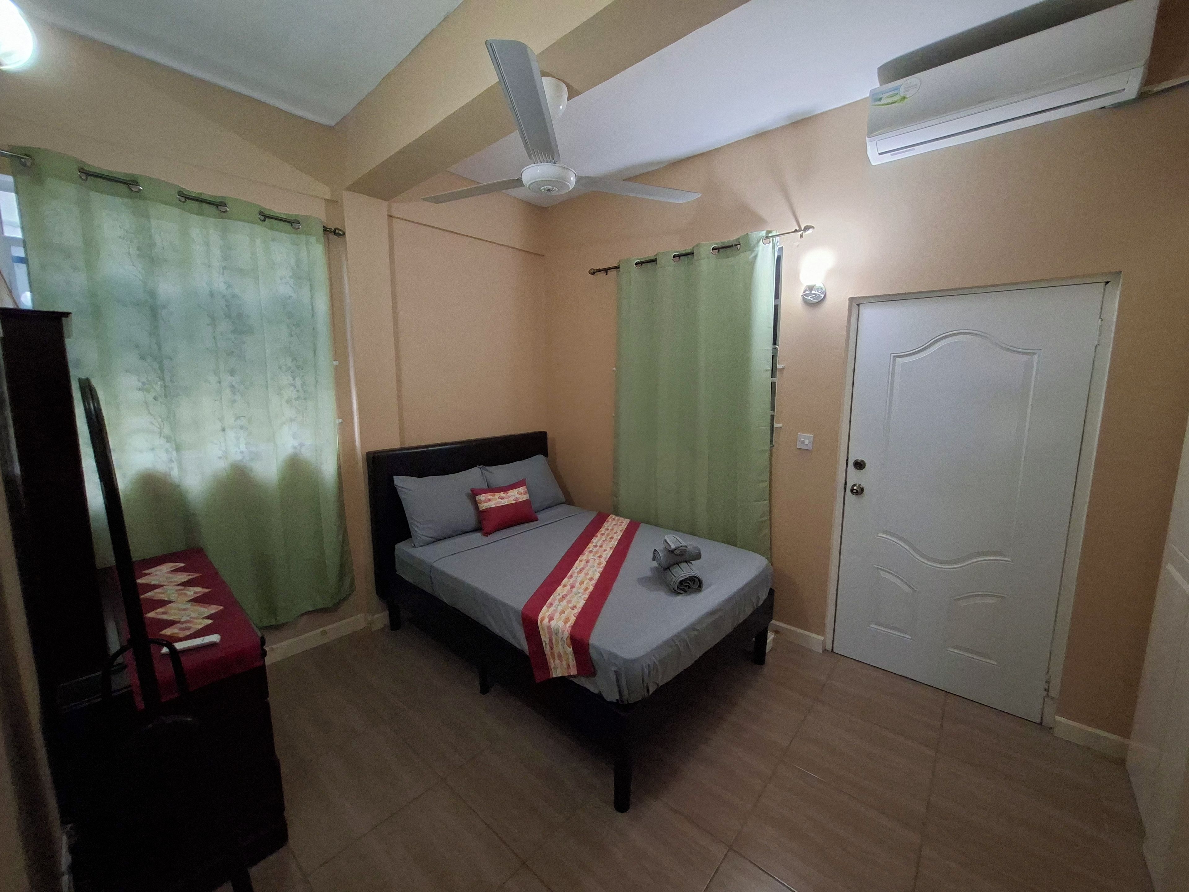 A bedroom with a bed, a ceiling fan, an air conditioning unit, a door, and curtains.