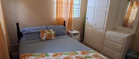 Un dormitorio con cama, armario, espejo, ventilador de techo y ventana con cortinas.