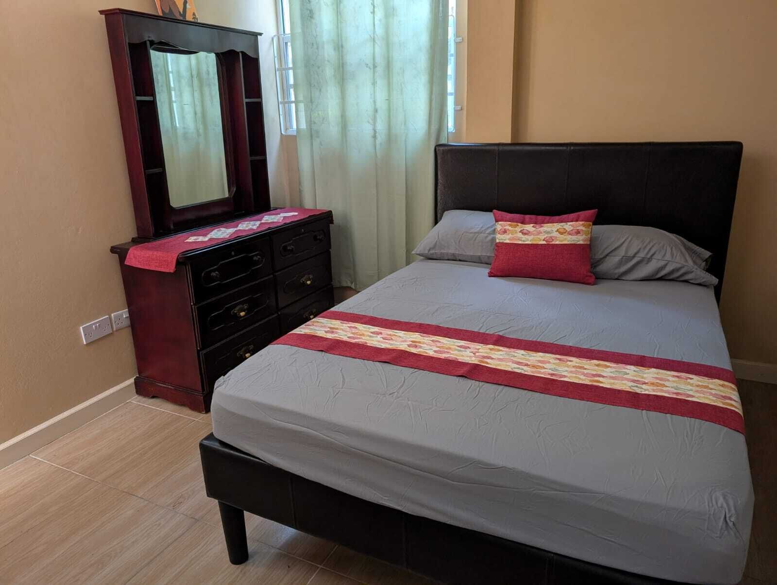 A bedroom with a bed, a dresser, a mirror, and a window with curtains.