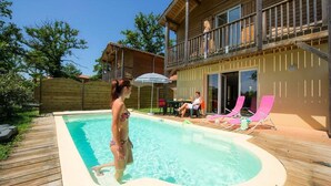 A wooden deck with a swimming pool, a covered patio, and a two-story building with a balcony. - Apartment in Eauze With Private Pool (Eauze)