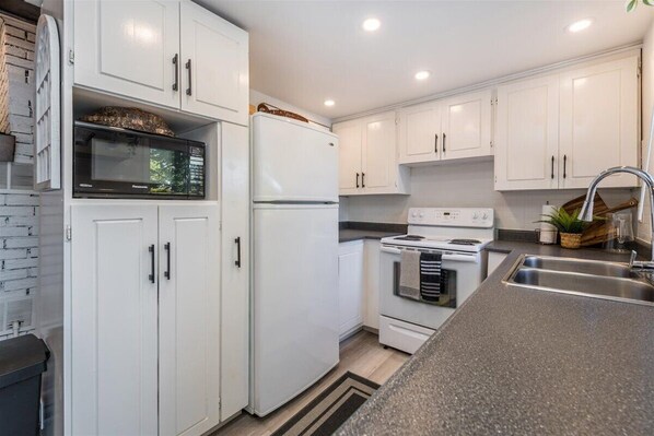 A modern kitchen with white cabinets, a built-in microwave, a refrigerator, a stove, and a sink. - Casa Albanese on Farlain Lake (Tiny)