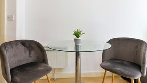 A modern room with a glass-top table, two dark chairs, a small potted plant, and a white radiator. - Modern 1 bed in Bow - Free Parking (London)