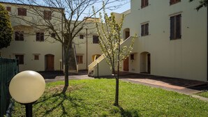 Ein Innenhof mit einem kleinen Baum, einem Laternenpfahl und einem Gebäude mit zahlreichen Fenstern und Türen.