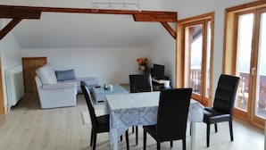 A dining area with a table set for four, surrounded by chairs, in a room with wooden beams on the ceiling and large windows. - Bella Vista Lodge (Kartitsch)