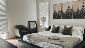 A bedroom with a bed, a chair, a bedside table, a lamp, and artwork on the wall. - Guest Favorite · Large Lux Rooftop Oasis House  · 4BR · Centrally Located! (Berry Hill)