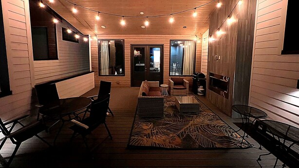 A cozy interior with wooden walls, a seating area with chairs and a sofa, a coffee table, and string lights on the ceiling. - Guest Favorite · Large Lux Rooftop Oasis House  · 4BR · Centrally Located! (Berry Hill)
