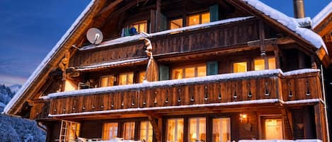 Un chalet de madera de varios pisos con balcones, techo cubierto de nieve y una chimenea.