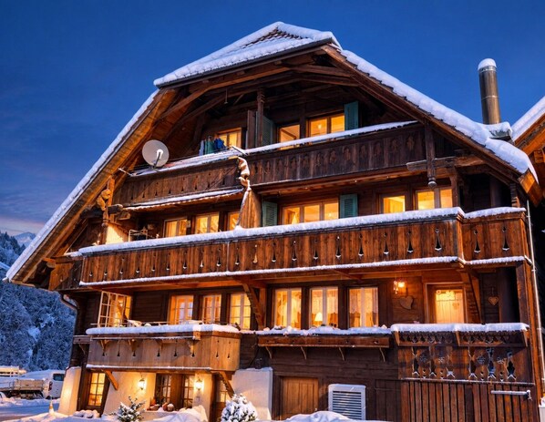 A multi-story wooden chalet with balconies, snow-covered roof, and a chimney.