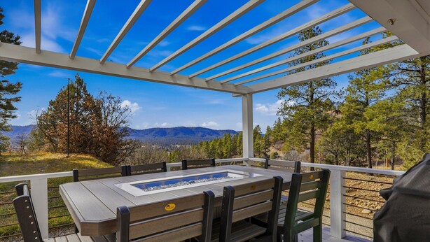 Un área de comedor al aire libre techada con una mesa y sillas, con vistas a un paisaje montañoso.