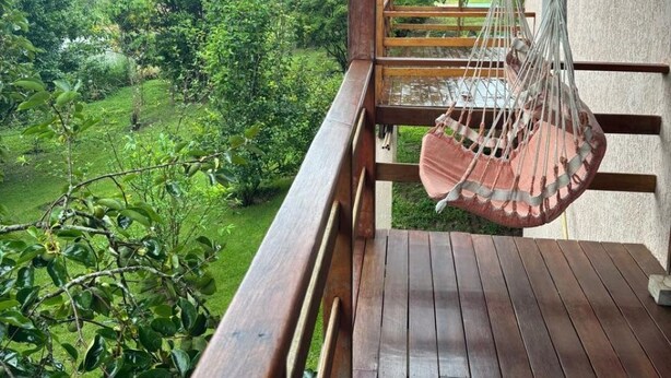 Una terraza de madera con una silla colgante con vistas a un jardín exuberante.