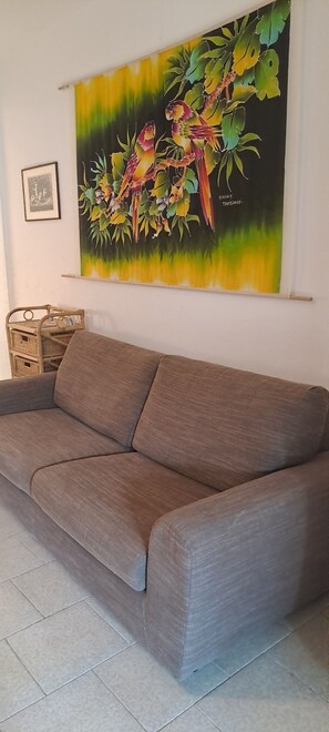 Un sofá gris en una habitación con un gran cuadro mural de aves y follaje.