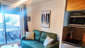 A living area with a green sofa, a small table, and a kitchen area with a microwave and dishwasher. - Les Marmottes Ndeg112 - ST5 (Chamrousse)