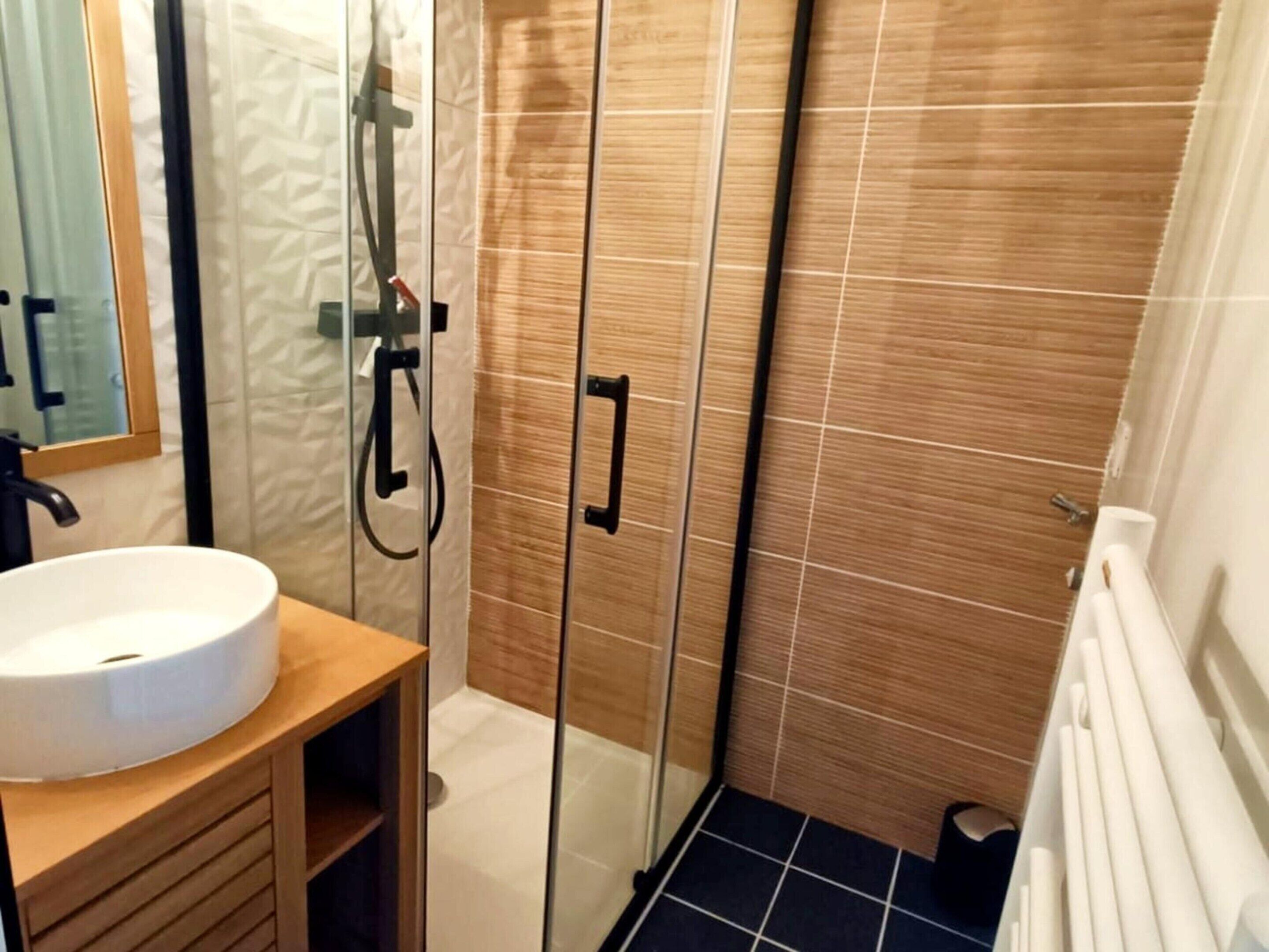 A bathroom with a white sink, wooden vanity, a glass shower enclosure, and tiled walls.