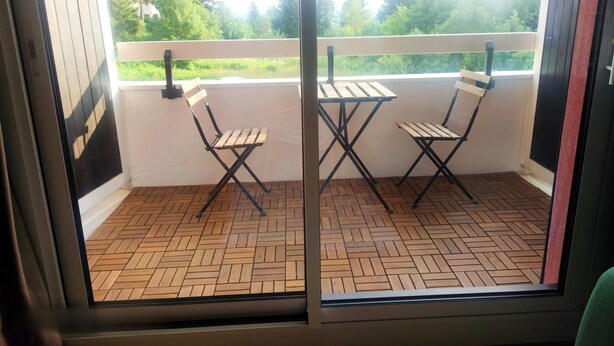 A balcony with two wooden folding chairs and a table, a herringbone-patterned floor, and a view of trees and greenery. - Les Marmottes Ndeg112 - ST5 (Chamrousse)