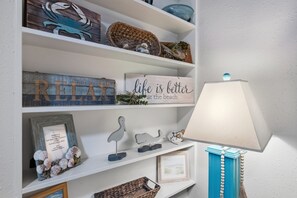 A shelf with decorative items including a sign that says "life is better at the beach," a framed welcome sign, and various small sculptures. - Gulf Village 201 | Sleeps 4 Beachfront West Beach (Gulf Shores)