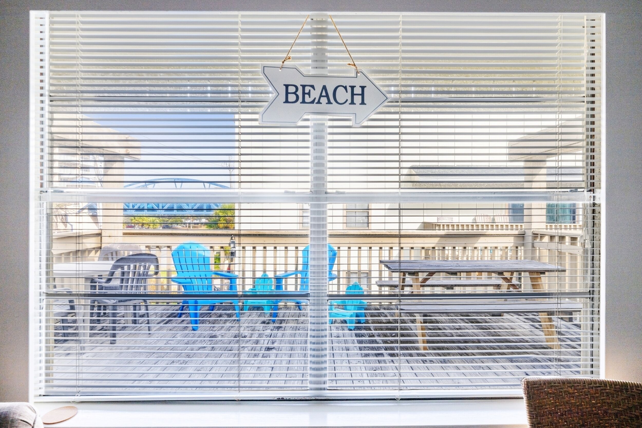 Vista pela janela, com uma placa indicando 'BEACH' e móveis de exterior.