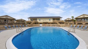 Una piscina circondata da lettini e ringhiere in legno, con un edificio sullo sfondo.