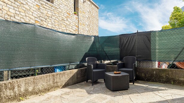 An outdoor patio with stone flooring, wicker furniture, and a green mesh screen. - La Dolce Vita - 500m da Menaggio centro (Menaggio)