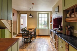 A kitchen with wooden cabinets, a dining table, chairs, a hanging light, and a window. - Stylish and Central Cottage Home in Montpelier (Bristol)