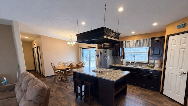 A modern kitchen with a central island, dark cabinetry, and a dining area with wooden chairs.