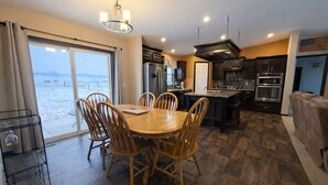 A modern kitchen with a dining area, large windows, and a view of the sea.