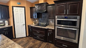 A kitchen with dark wood cabinets, a white door, granite countertops, and stainless steel appliances.