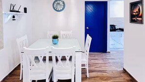 Ruokailutila, jossa on valkoinen pöytä ja tuolit, koristeellinen valaisin ja taustalla sininen ovi.