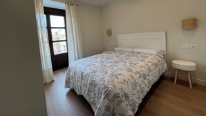 Un dormitorio con cama, mesita de noche, lámpara de pared y ventana con cortinas.