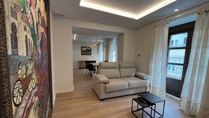 Una sala de estar moderna con un sofá color crema, una mesa de centro y un área de comedor al fondo.