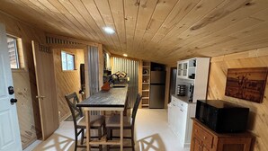 Kompakti keittiö, jossa on puiset kaapit, ruokapöytä tuoleineen, jääkaappi ja mikroaaltouuni.