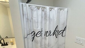 A bathroom with a shower curtain featuring a "get naked" text and a leaf pattern.