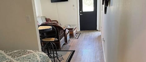 Ein Flur, der zu einem Schlafzimmer führt, mit einem Bett, einem Deckenventilator, einem Fernseher und einer Tür mit der Aufschrift 'LAKE OKOBOI'.
