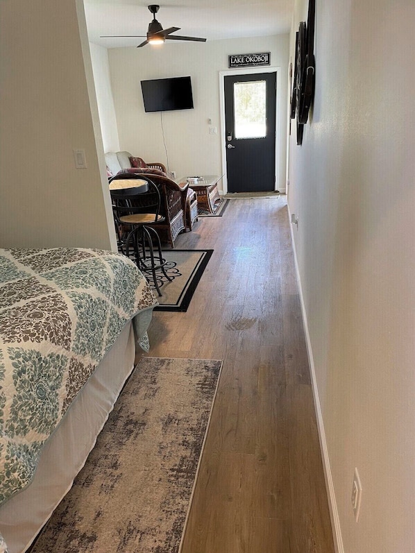 Un couloir mène à une chambre qui contient un lit, un ventilateur de plafond, un téléviseur et une porte sur laquelle est inscrit « LAC OKOBOI ».