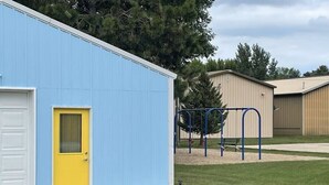 A blue building with a yellow door, a white garage door, and a playground with blue equipment.