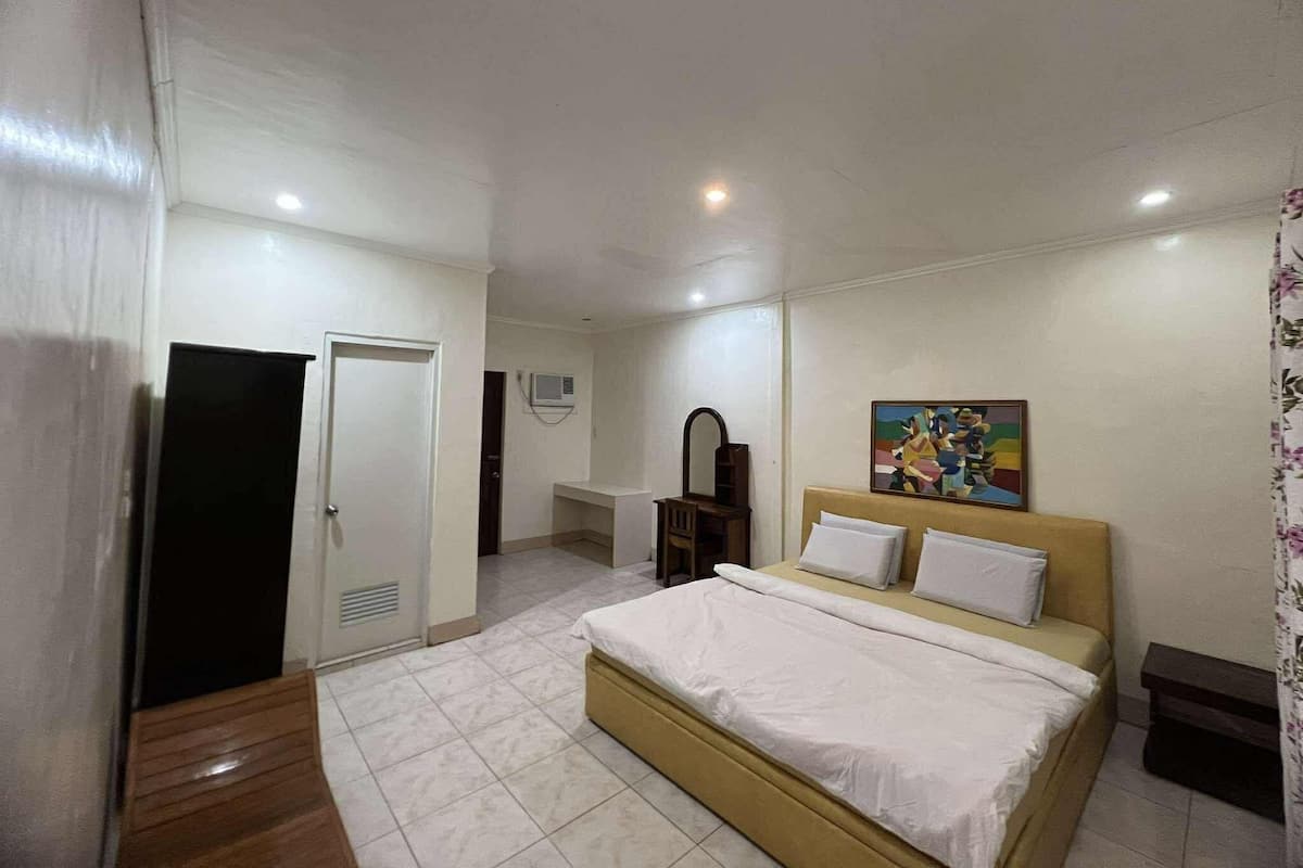 A bedroom with a bed, a door, a mirror, a painting, and a small table.