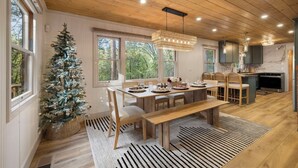 Una cocina moderna con armarios de madera, un comedor con una mesa grande y bancos, y un árbol de Navidad.