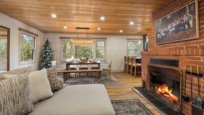 Una sala de estar acogedora con chimenea, techo de madera y un comedor con árbol de Navidad.